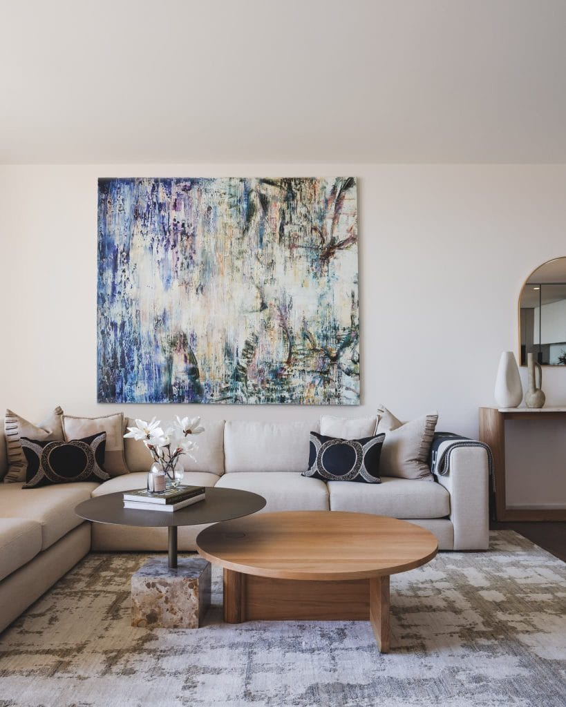 A modern living room with a beige sectional, black pillows, round coffee tables, and an abstract painting.