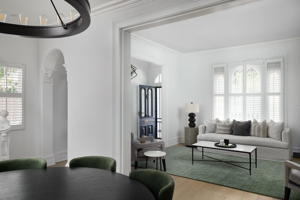 A modern living room with a white sofa, green rug, and black table is seen from a dining area; Emma Blomfield is present.