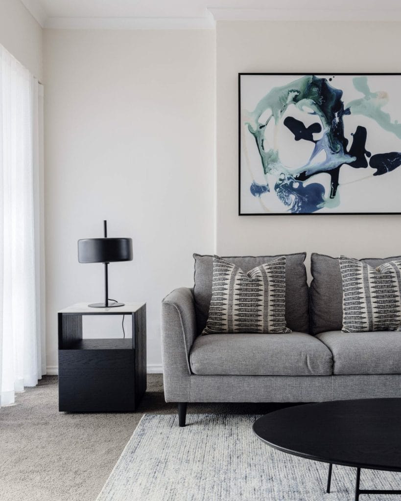 A modern living room with a grey sofa, patterned cushions, abstract art, and if present, Emma Blomfield sitting nearby.