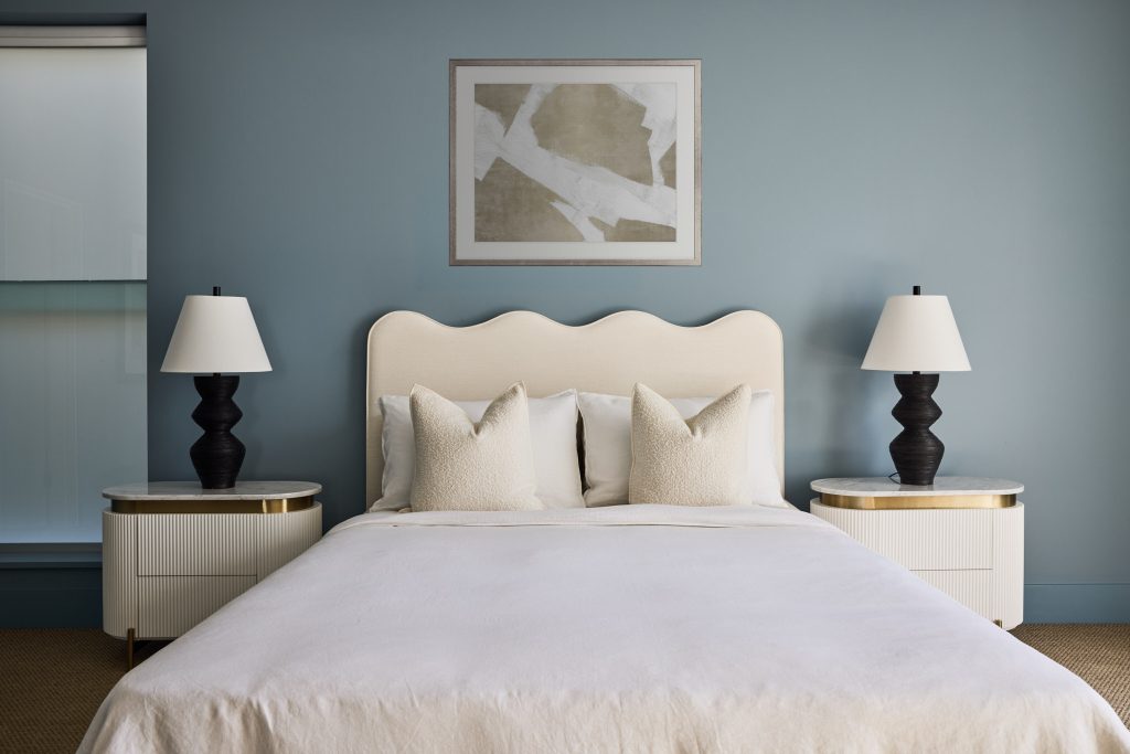 A modern Beauty Point Home bedroom features a double bed, two pillows, matching side tables and lamps, and abstract art on a blue wall.