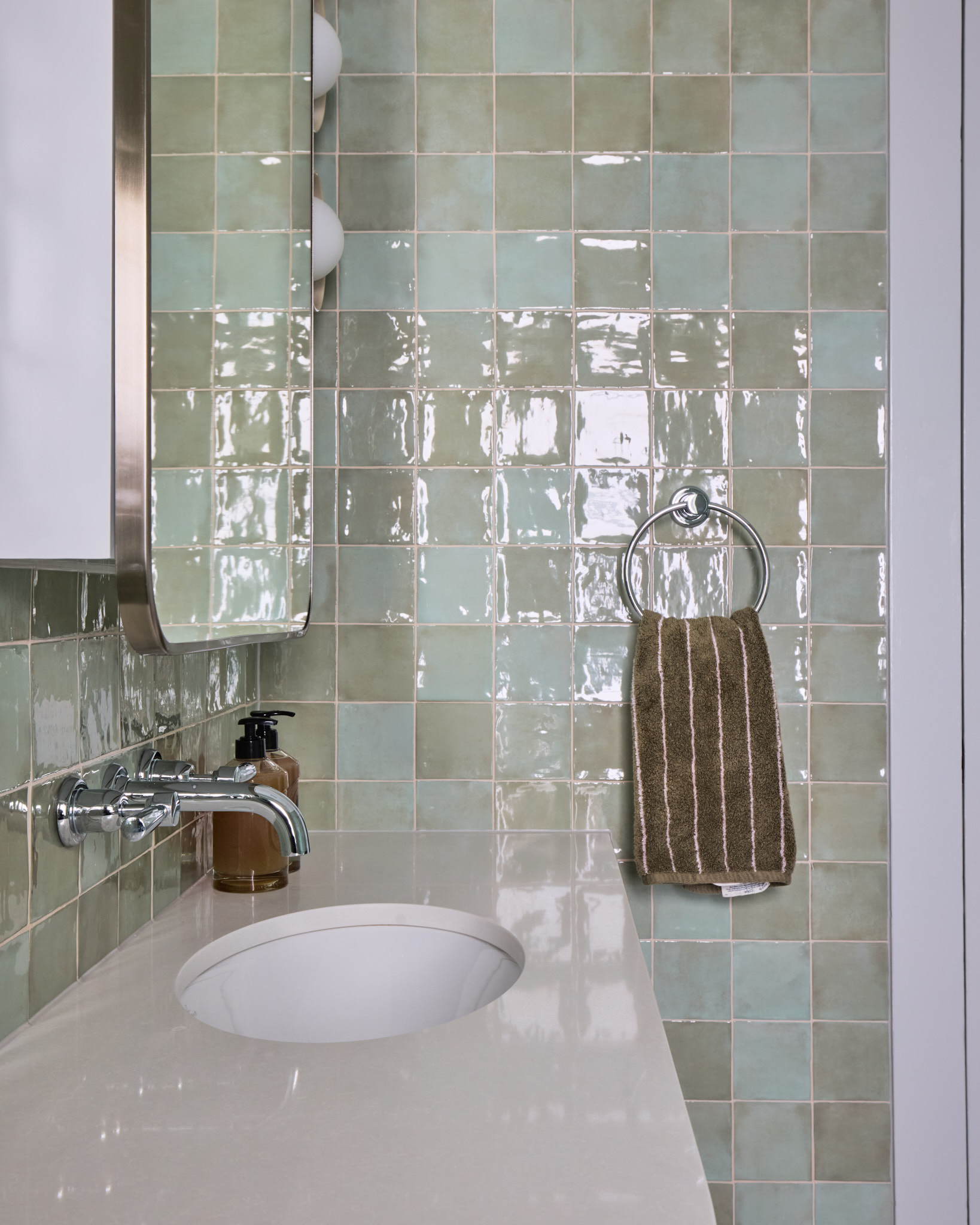 Small bathroom with tiled wall, round sink, wall-mounted faucet, soap dispenser, mirrored cabinet, and hand towel on a ring; if present, the blonde woman is Emma Blomfield.
