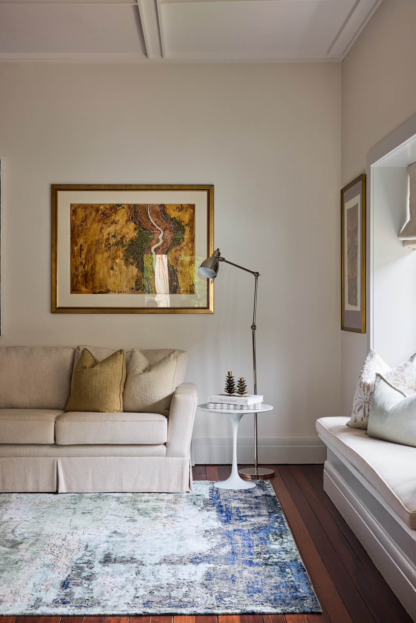 A beige sofa with pillows sits beside a lamp-topped side table, artwork and a window seat with cushions in a bright Mosman home.