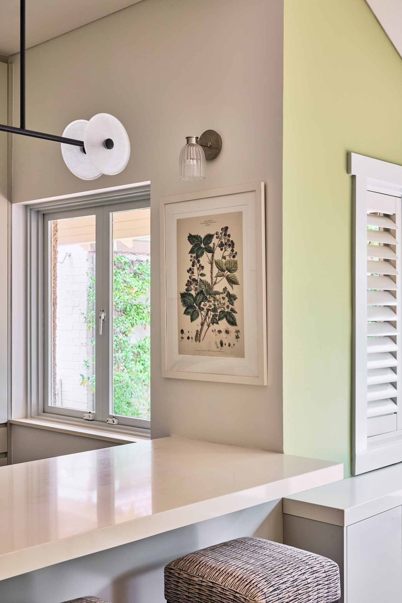Modern kitchen with white countertop, two woven stools, a window, botanical wall art, and light gray and green walls—a chic Mosman home update.