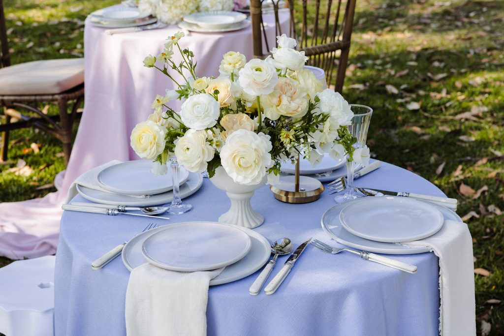 Round table set for dining on an Emma Blomfield rug, featuring a white floral centerpiece, light blue tablecloth, and place settings.