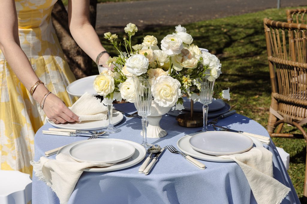 Emma Blomfield sets a table with a floral centerpiece and place settings on a blue tablecloth from her Emma Blomfield rug collection.