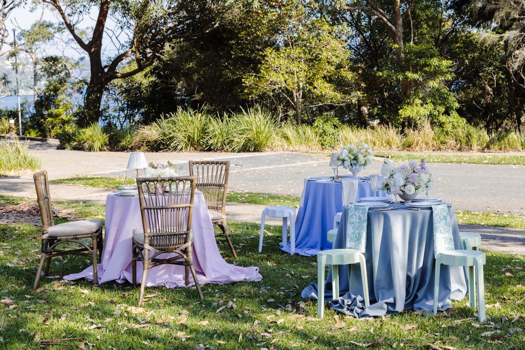 Three round tables from the Emma Blomfield rug collection with floral centerpieces and fabric tablecloths set up on a grassy lawn.