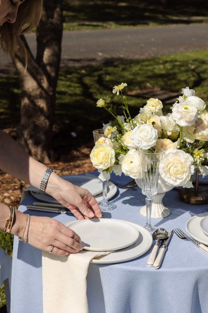 Emma Blomfield sets a plate on a table atop an Emma Blomfield rug, decorated with a floral centerpiece and place settings.