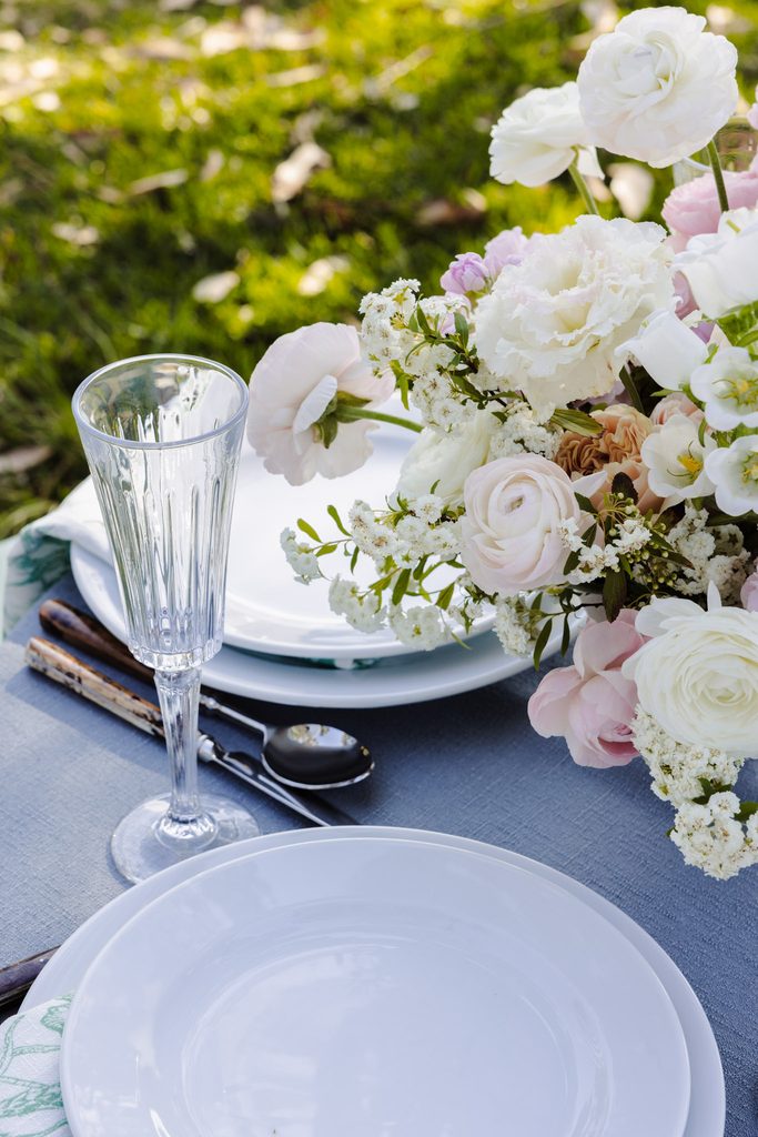 A place setting on a blue Emma Blomfield rug with a crystal flute and a floral centerpiece.