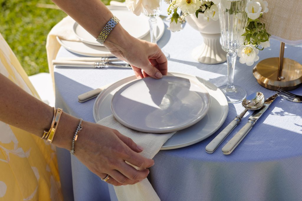 Emma Blomfield sets stacked ceramic plates and a napkin on a blue tablecloth from the Emma Blomfield rug collection.