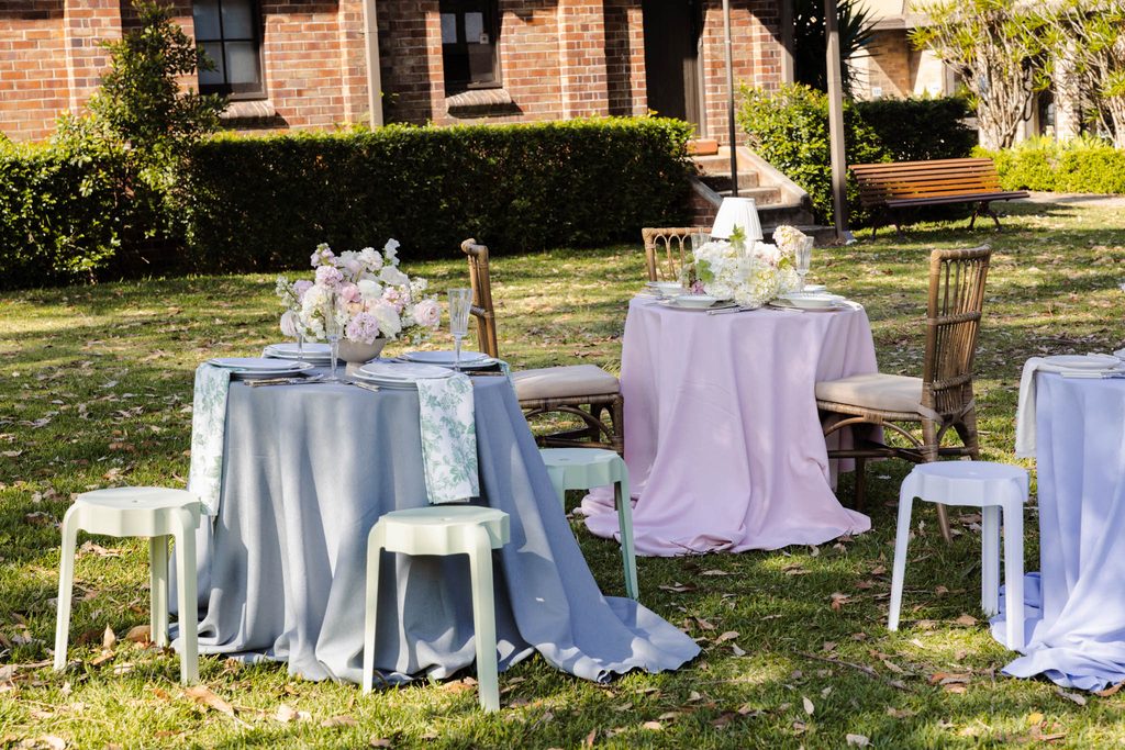 Pastel-covered round tables with floral centerpieces sit on an Emma Blomfield rug on the lawn.