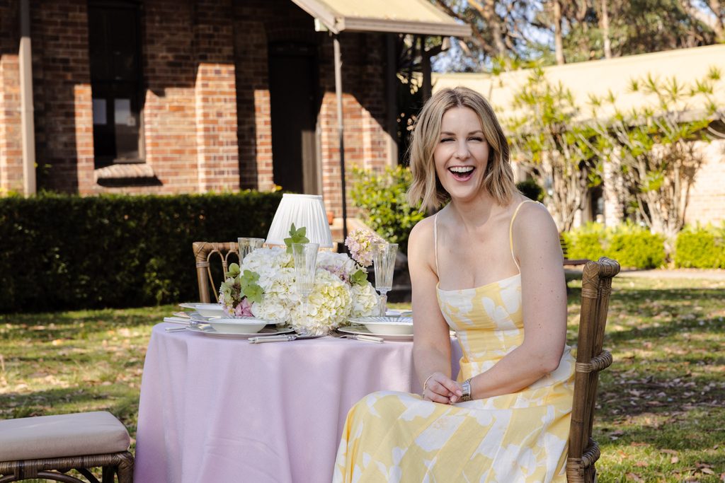 Emma Blomfield laughs while sitting at a garden table featuring pieces from the Emma Blomfield rug collection.